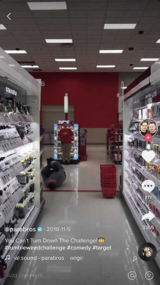A person lies on the floor of a store aisle, possibly filming a TikTok, while another stands in the background near a display.