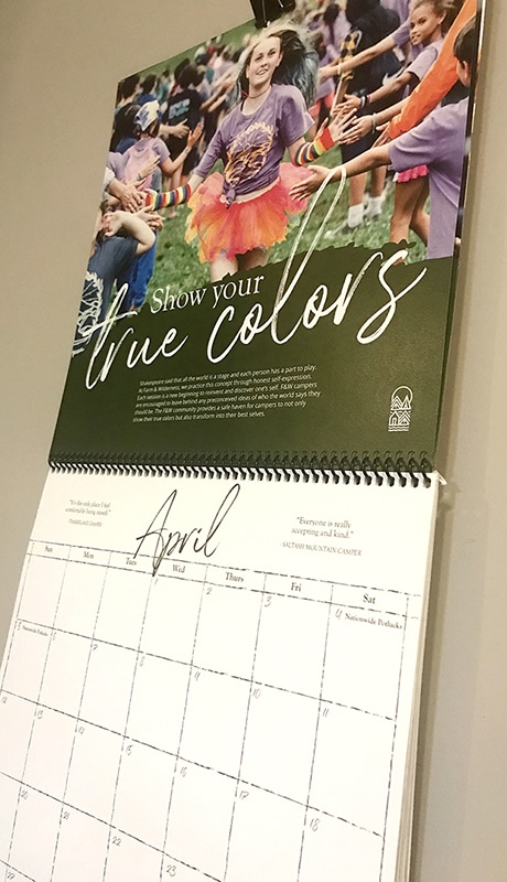 A wall calendar open to April, featuring a joyful group in colorful attire and the words Show your true colors—a perfect highlight for any Summer Camp Ad Campaign.