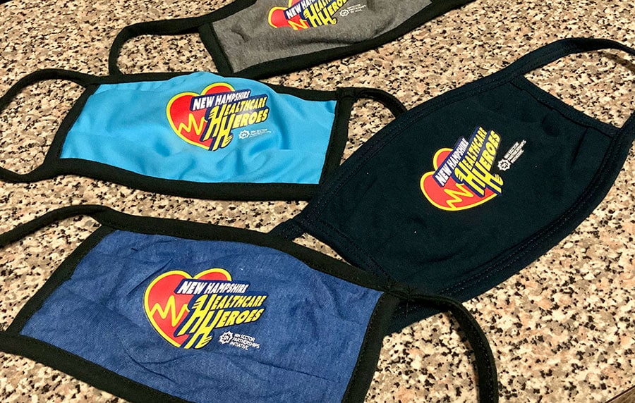 Four face masks on a granite surface, each featuring New Hampshire Health Care Heroes with a heart logo—perfect for healthcare branding.