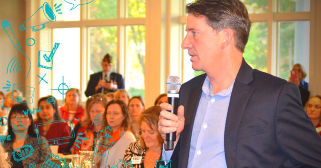 Man in a suit speaking into a microphone to a seated audience in a bright room, with blue doodle graphics overlay, highlighting the importance of media relations.