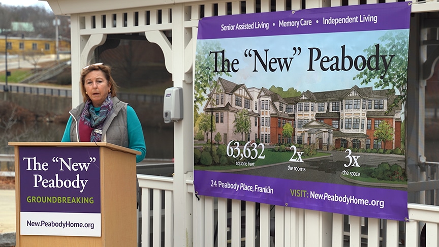 A woman speaks at a podium next to a banner for the new Peabody senior living facility in Franklin, highlighting its recent rebranding.