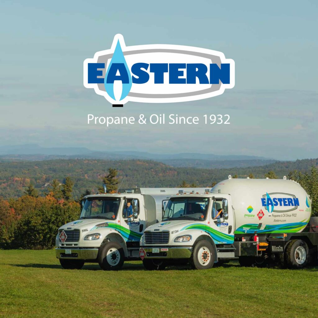 Two Eastern propane delivery trucks parked on grass with mountains and trees in the background.