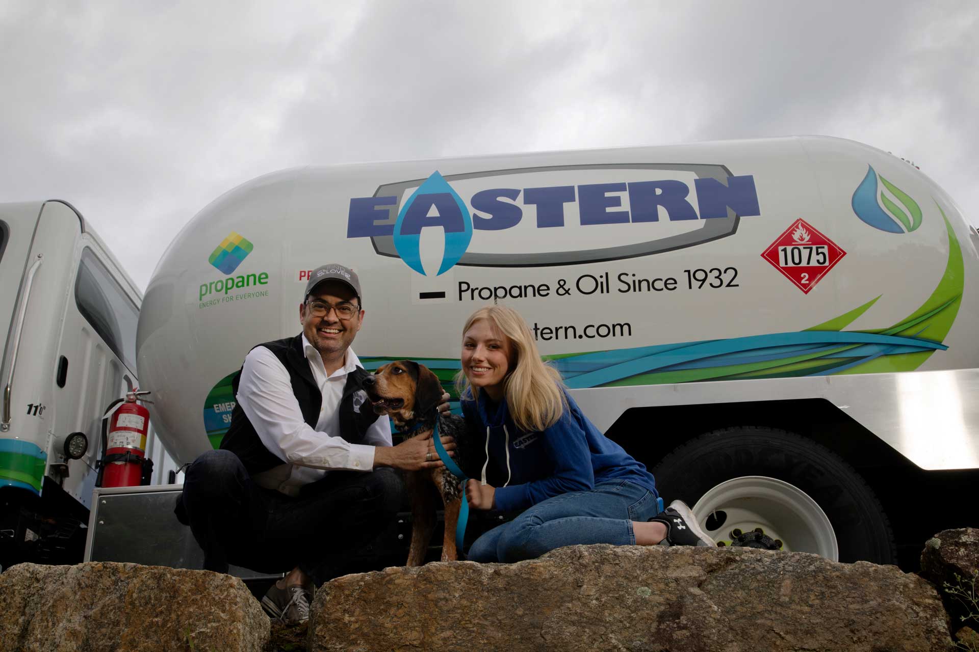 A man, woman, and dog pose in front of an Eastern propane truck on a cloudy day.