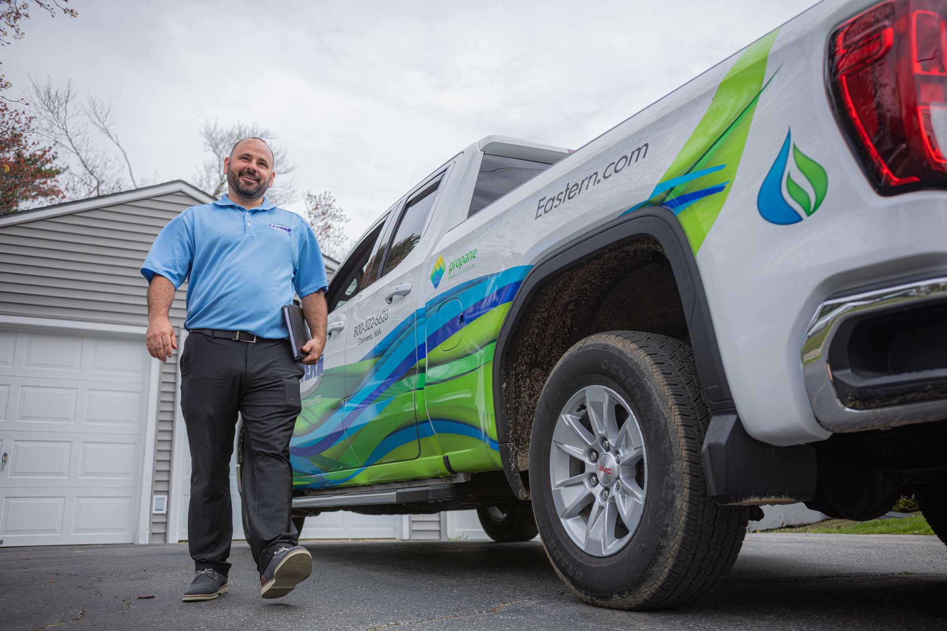 Smiling man in polo shirt walks beside a branded company pickup truck parked in a driveway.