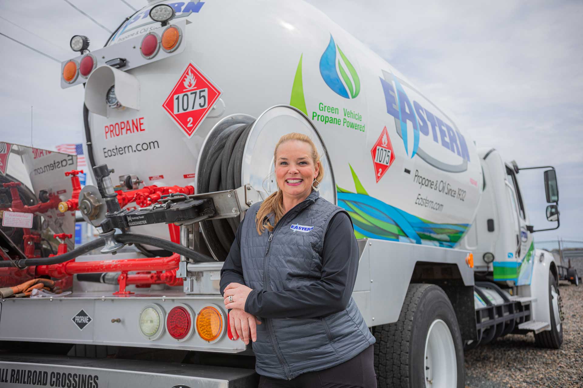 Smiling woman stands in front of a propane delivery truck labeled Eastern in an outdoor lot.
