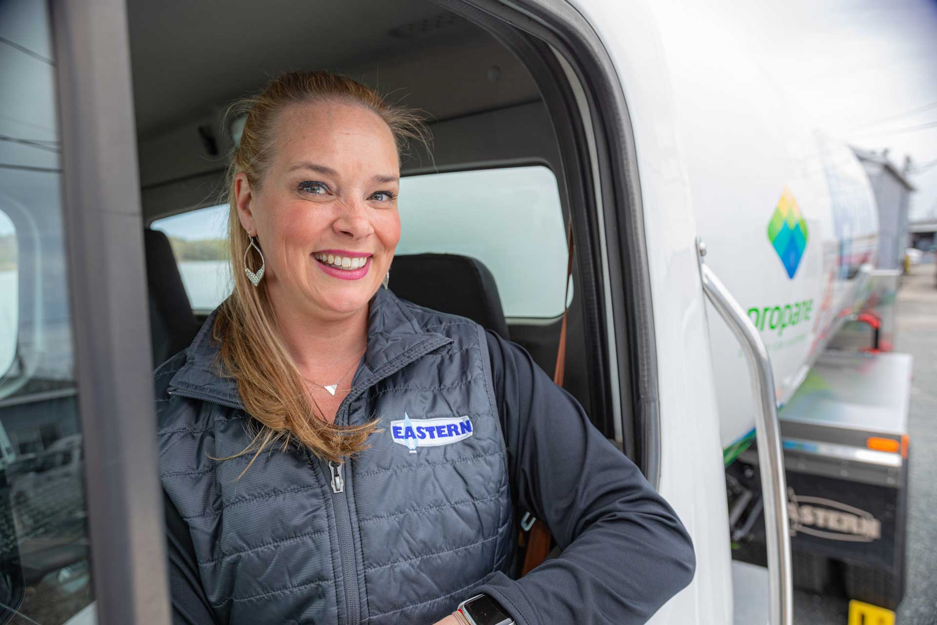 Smiling woman in an Eastern jacket stands at the open door of a propane delivery truck.