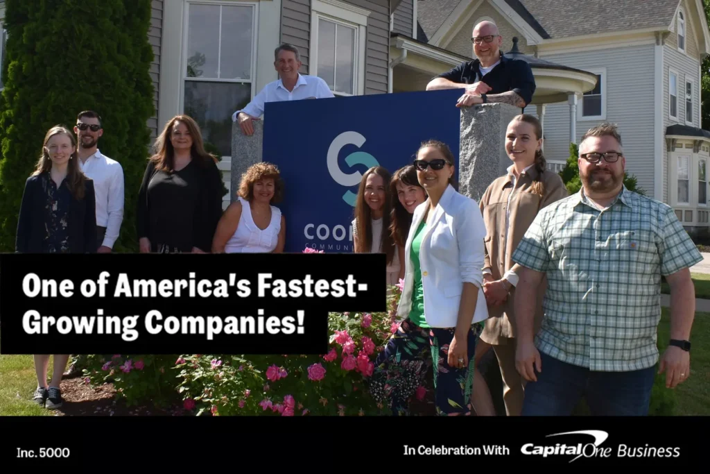 A group of people smiling outside beside a sign that reads “One of America’s Fastest-Growing Companies!”.