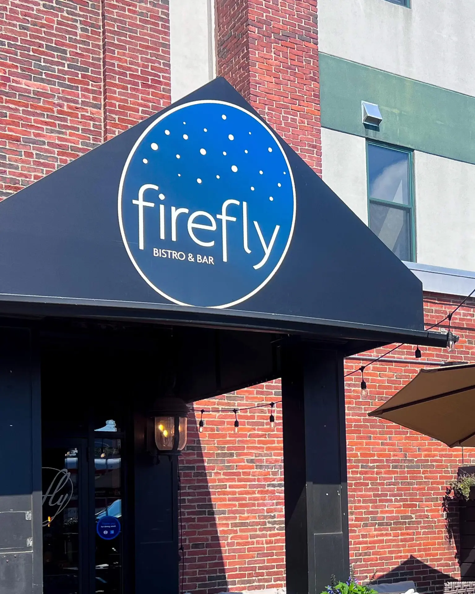 Blue circular sign with firefly BISTRO & BAR above the entrance of a brick building.
