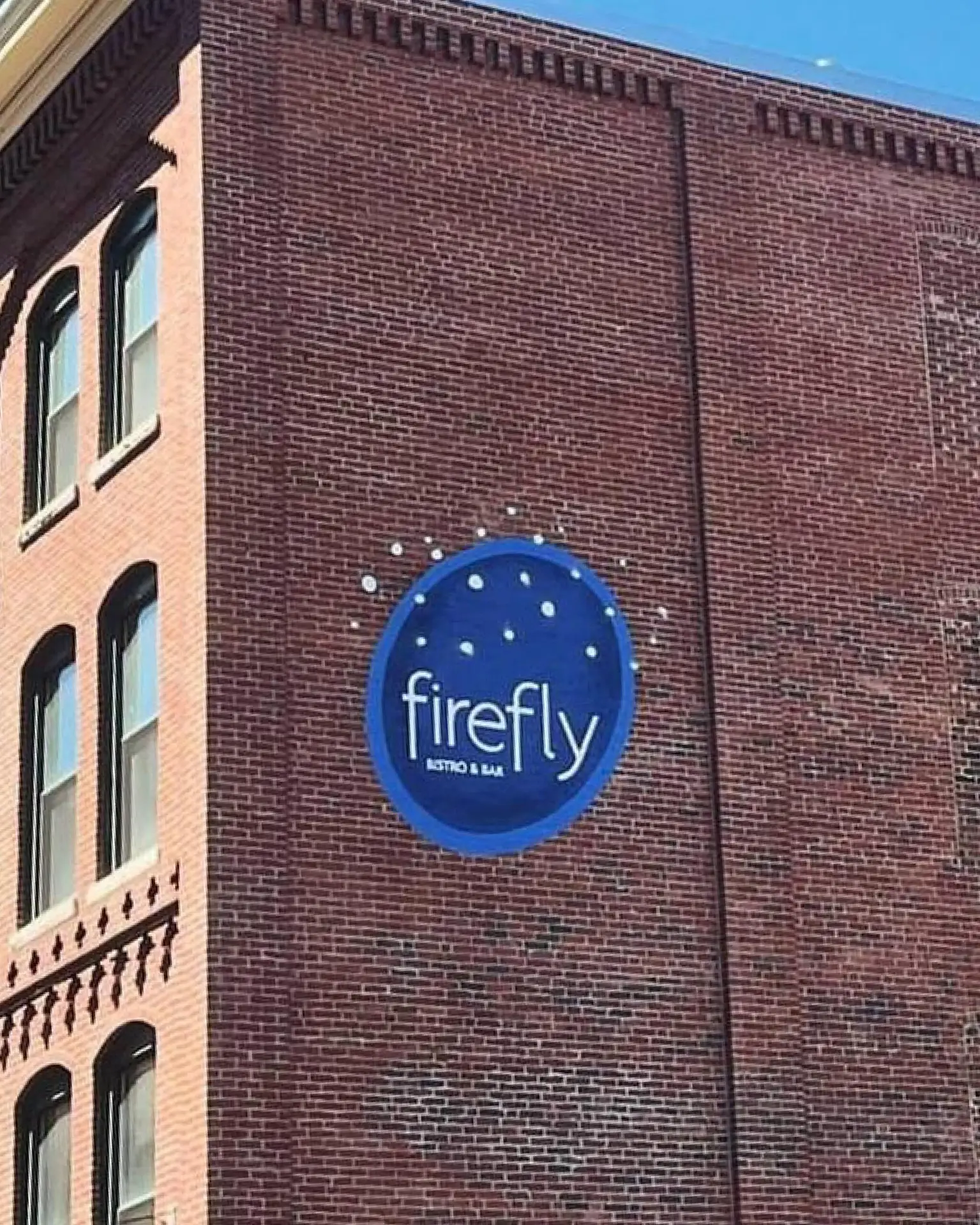 A round firefly bistro & bar sign on the brick exterior of a building.