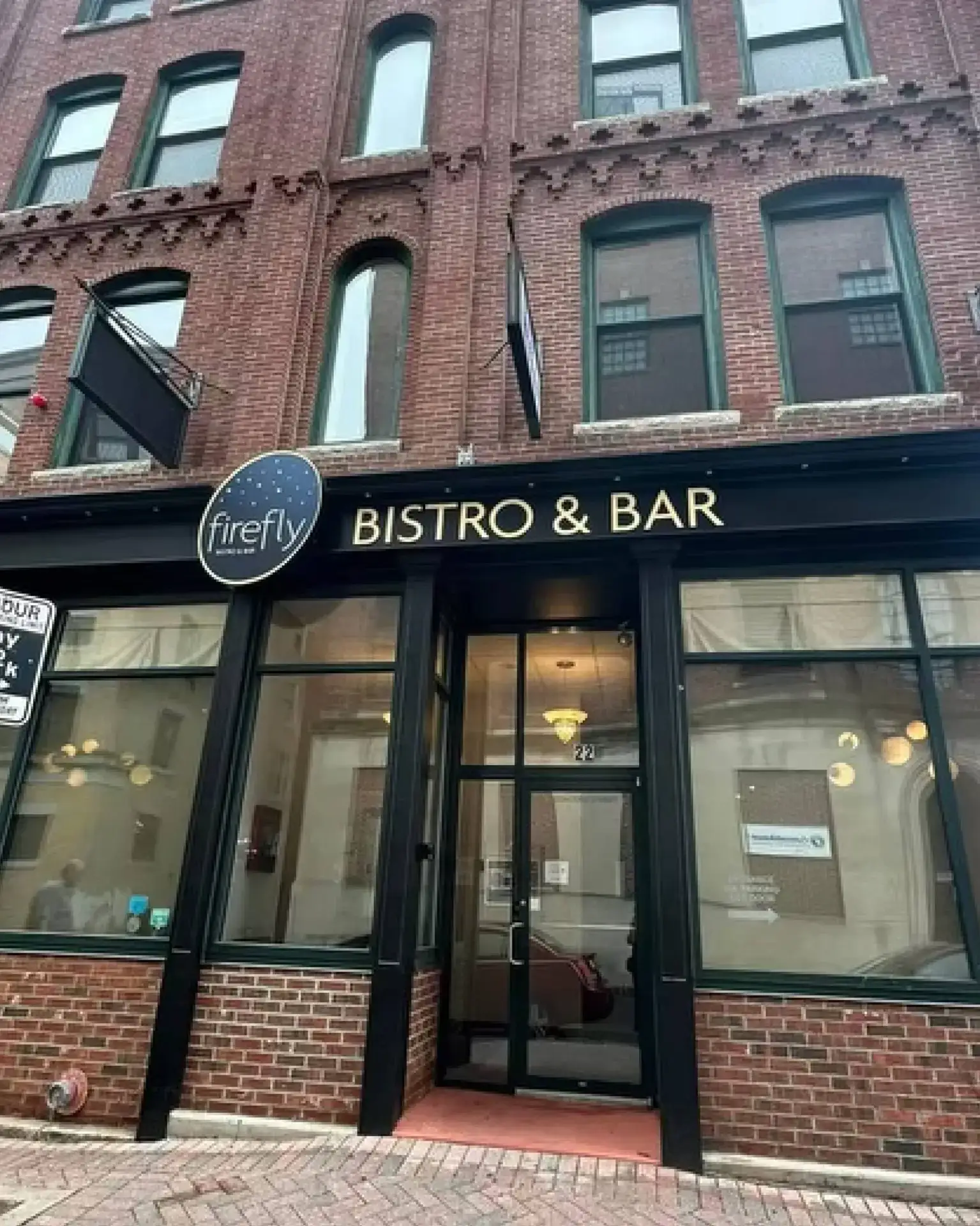 Storefront of Firefly Bistro & Bar with large windows in a brick building on a city street.