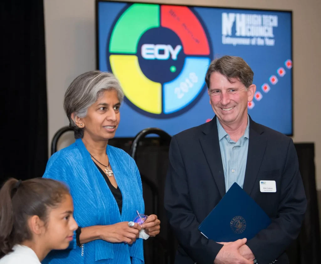 Two adults engaged in conversation at an event, with a colorful EOY 2018 logo displayed on a screen in the background—highlighting the impact of non-profit communications.