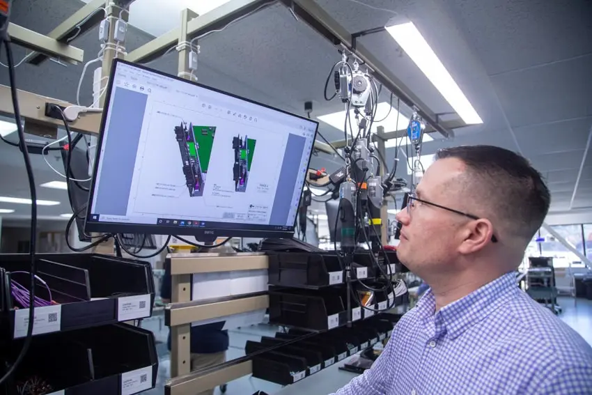 Man in glasses examines technical diagrams on a large computer monitor in an electronics lab, focusing on manufacturing website design solutions.