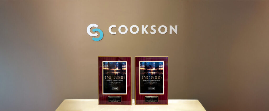 Two INC. 5000 award plaques on a table beneath the Cookson company logo on a beige wall.