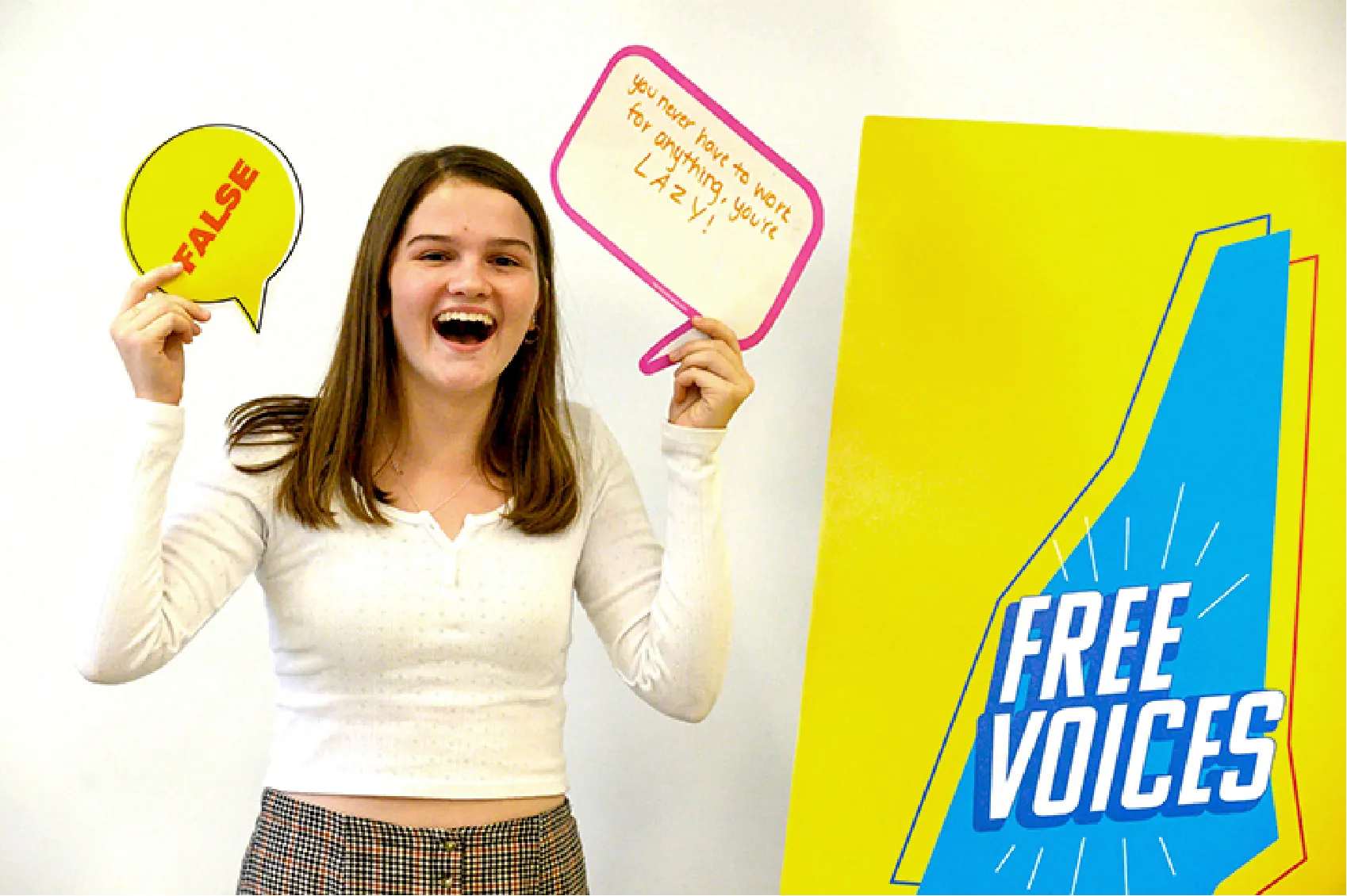 Smiling girl holds a FALSE bubble and a sign near a bright yellow FREE VOICES display.