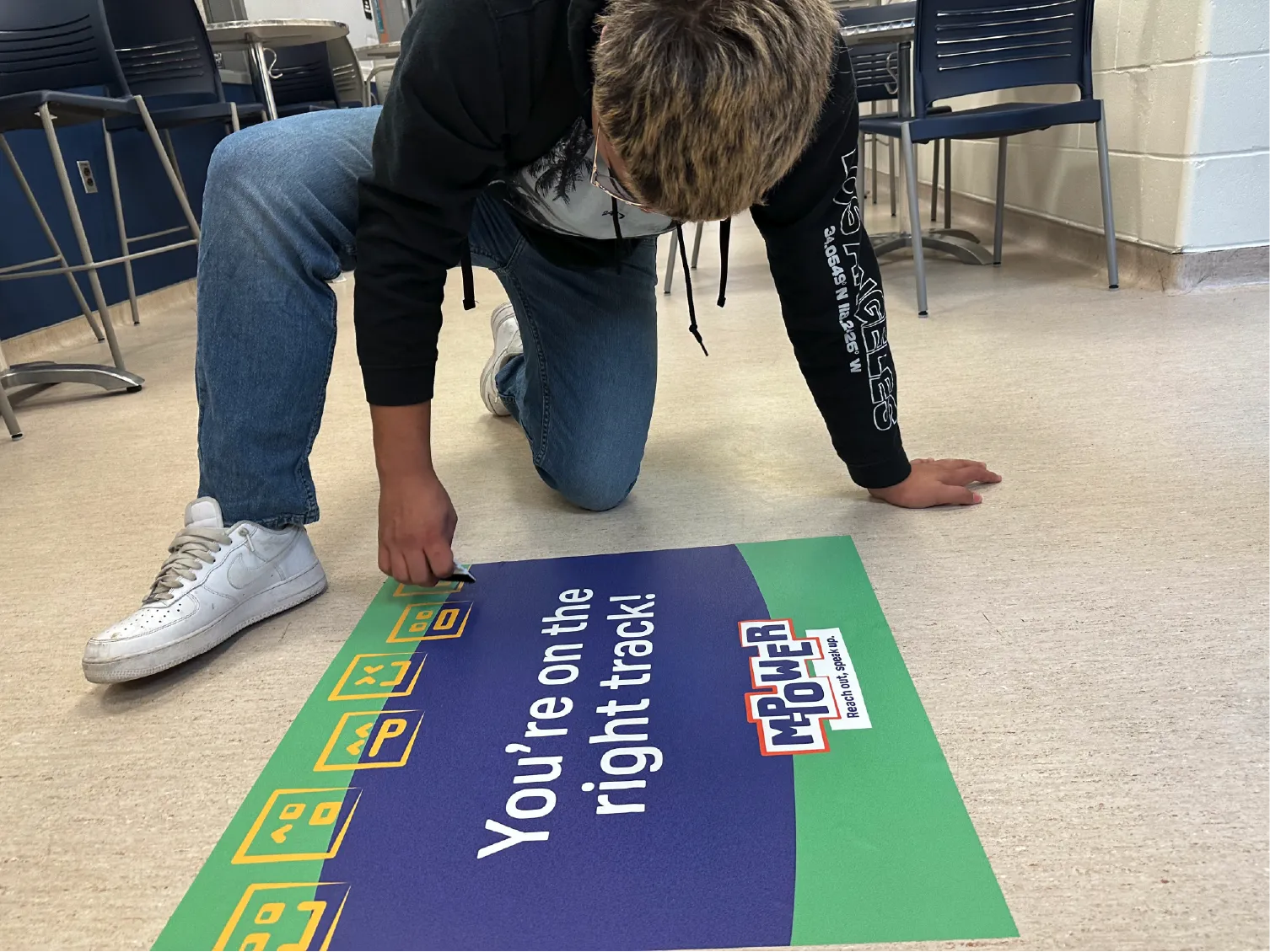 Person kneeling on floor, placing a sign that says, You’re on the right track! with a Mower County logo.