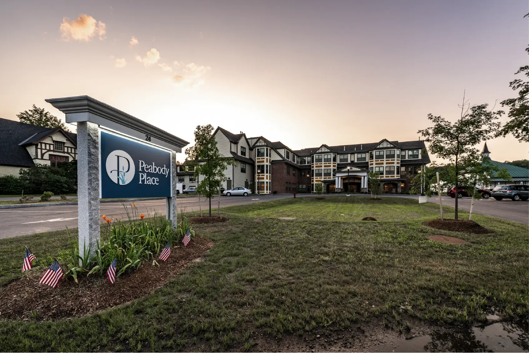 Peabody Place sign and building at sunset, with small US flags and flowers along the lawn, reflecting a strong sense of Community.