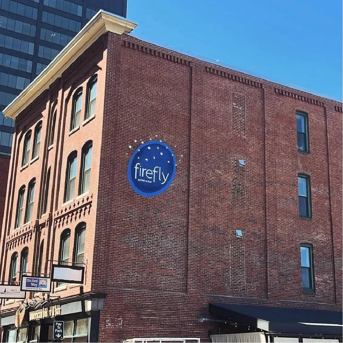 A brick building with a blue firefly sign on its side, set against a clear blue sky, stands as a vibrant hub for community gatherings and creative marketing efforts.