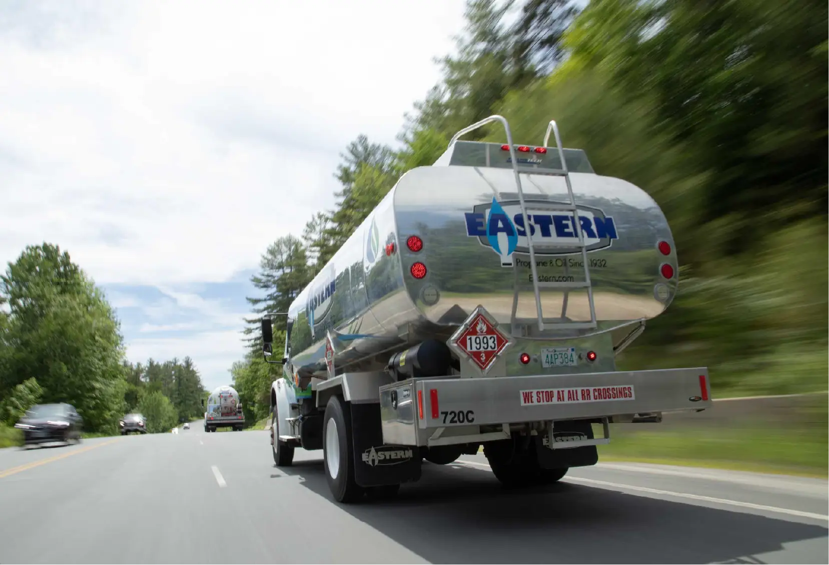 A shiny fuel truck labeled EASTERN drives down a tree-lined road on a sunny day, showcasing community spirit while serving as a rolling marketing presence.
