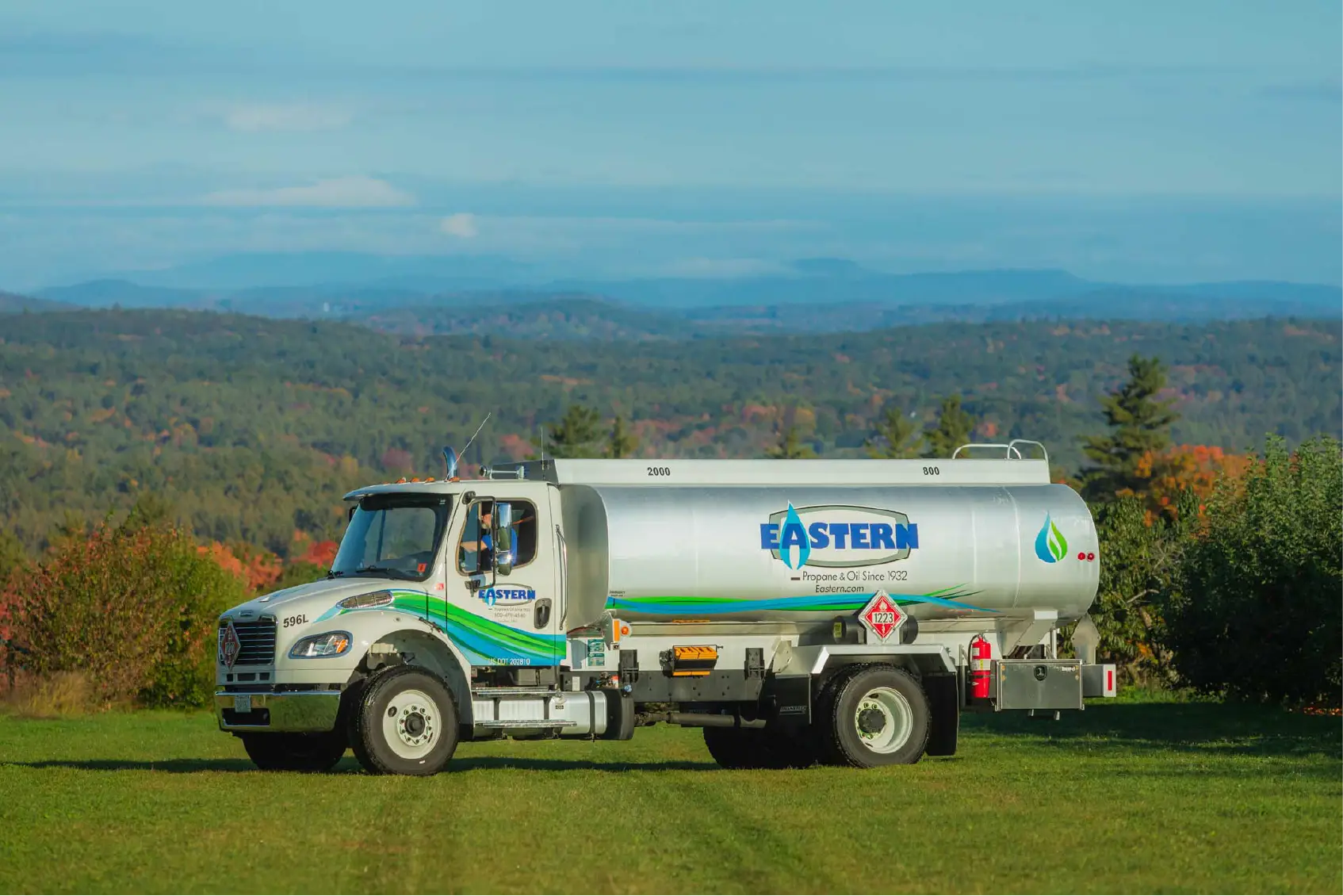 A silver Eastern propane delivery truck, used for local marketing, is parked on grass with hills and trees in the background, serving the community.
