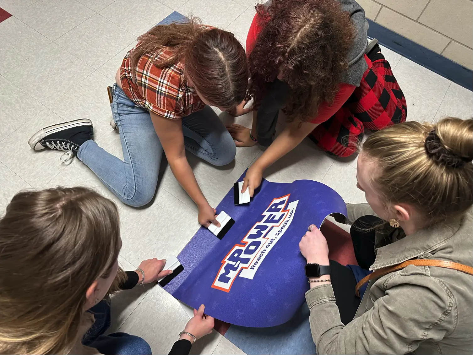 Four people kneel on the floor, inserting cards into a box labeled My POWER: Pride, Ownership, Wisdom—a powerful scene of community and collective spirit.