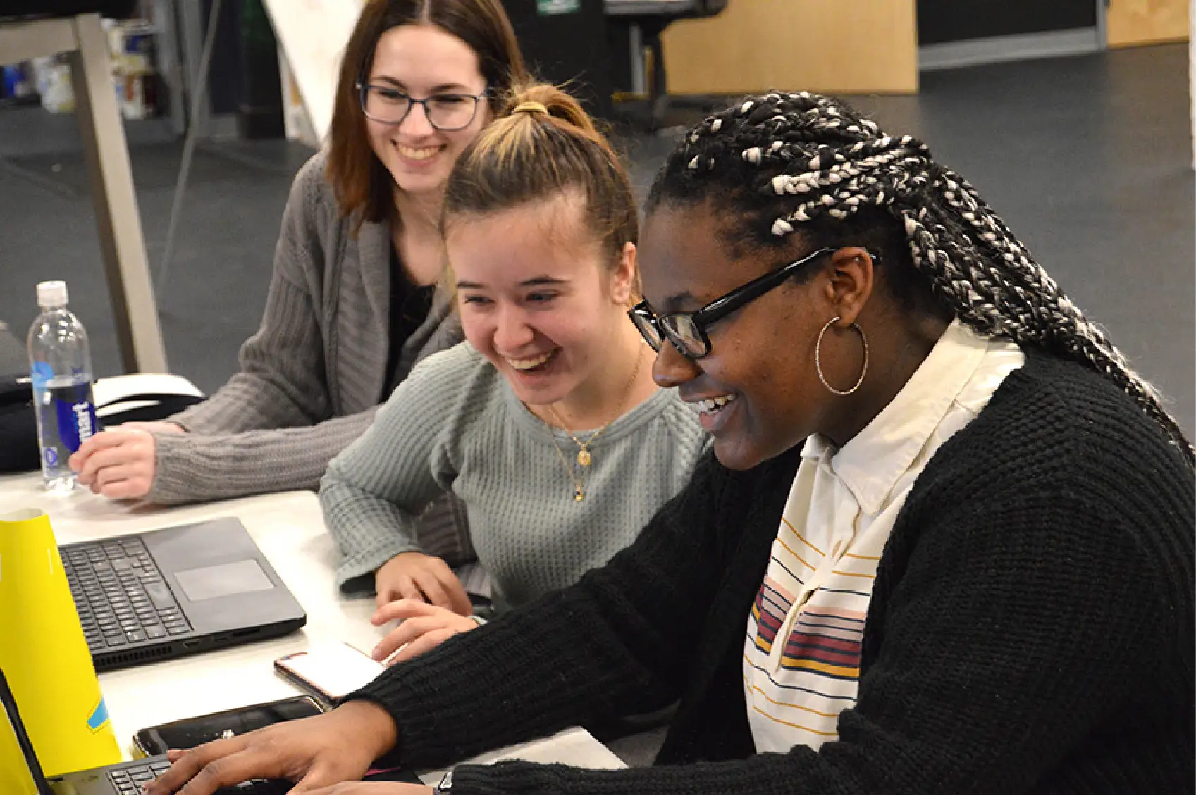 Three young women sitting at a table, smiling and working together on laptops, showcasing the power of community in marketing.