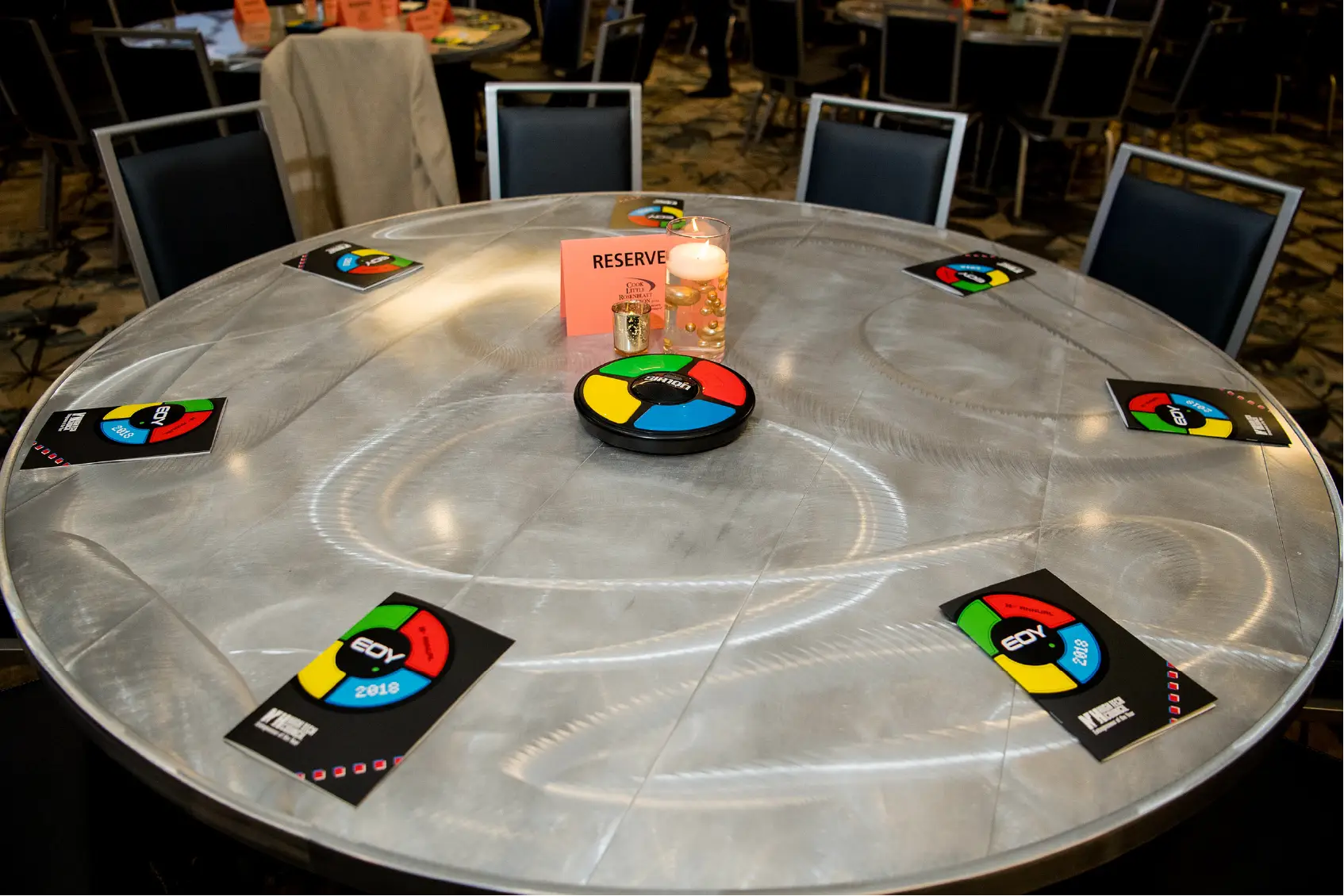 A round table with a Reserved sign, Simon games, and cards set for an event, surrounded by chairs.
