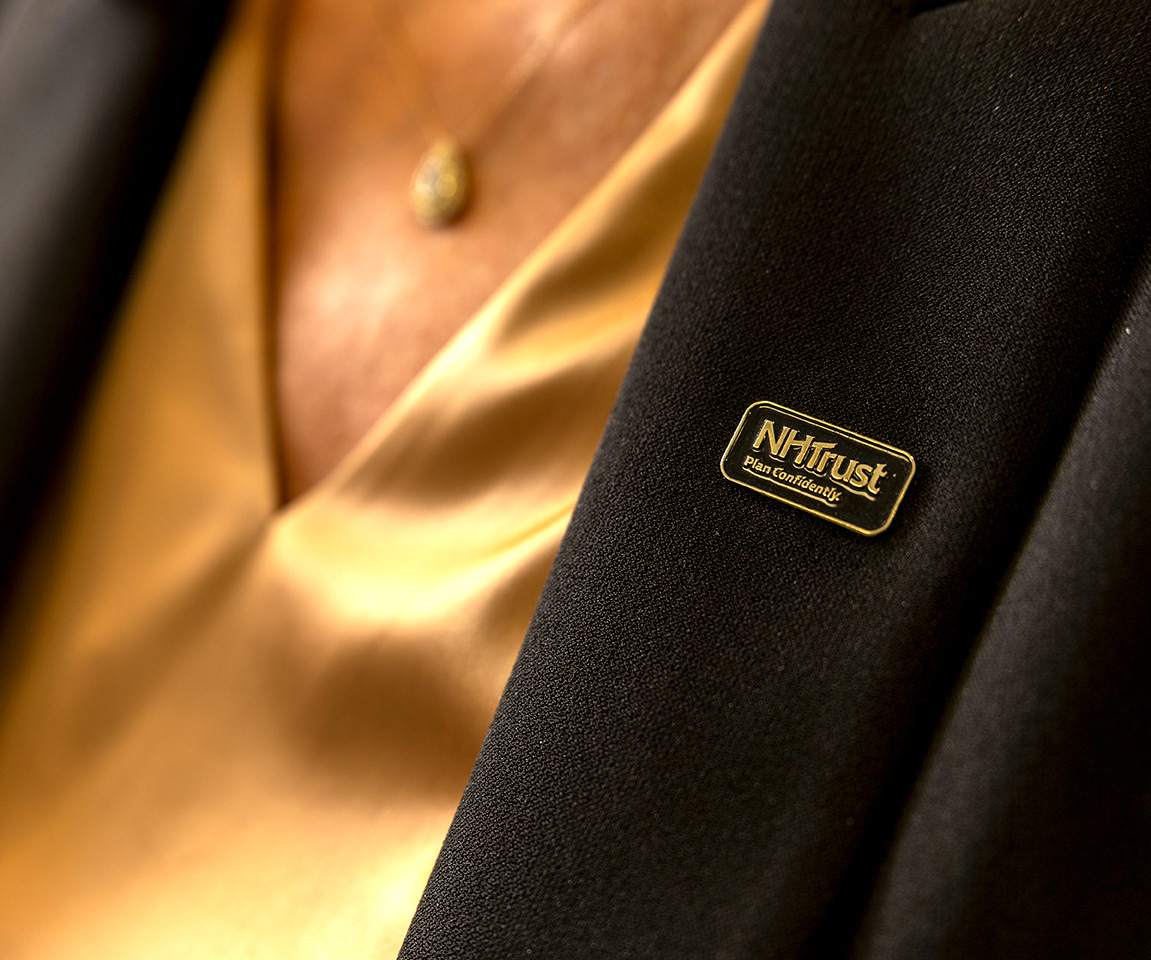 A person wearing a gold shirt and a black blazer with an NHTTrust name badge, presenting a polished look suited for tech or finance professionals.