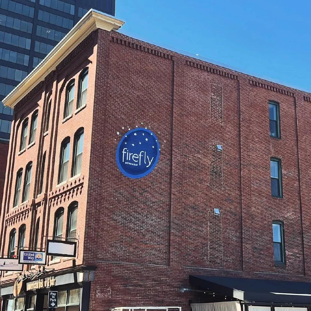 A red brick building with a large blue firefly sign, showcasing thoughtful brand strategy, stands tall against a clear blue sky.