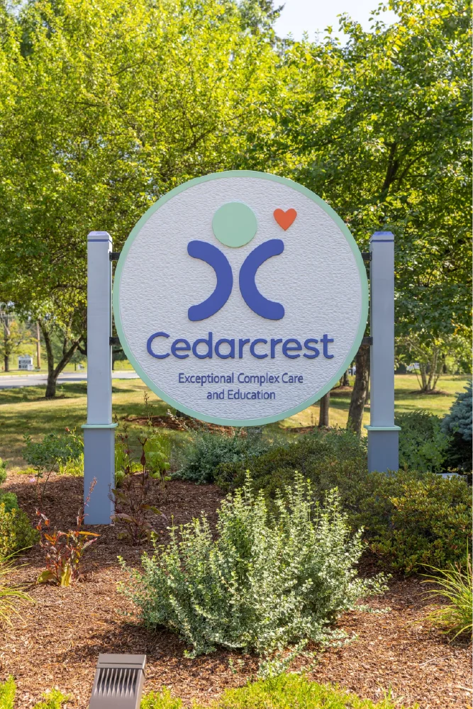 Round Cedarcrest sign in a garden reads Exceptional Complex Care and Education with a heart logo, reflecting the organization’s thoughtful brand strategy.