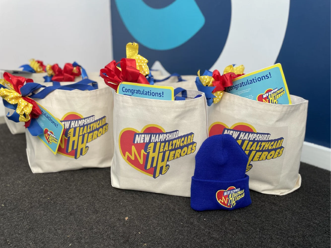 Gift bags featuring New Hampshire Healthcare Heroes logos showcase thoughtful brand strategy, complete with gift cards and a blue beanie on a dark carpeted floor.
