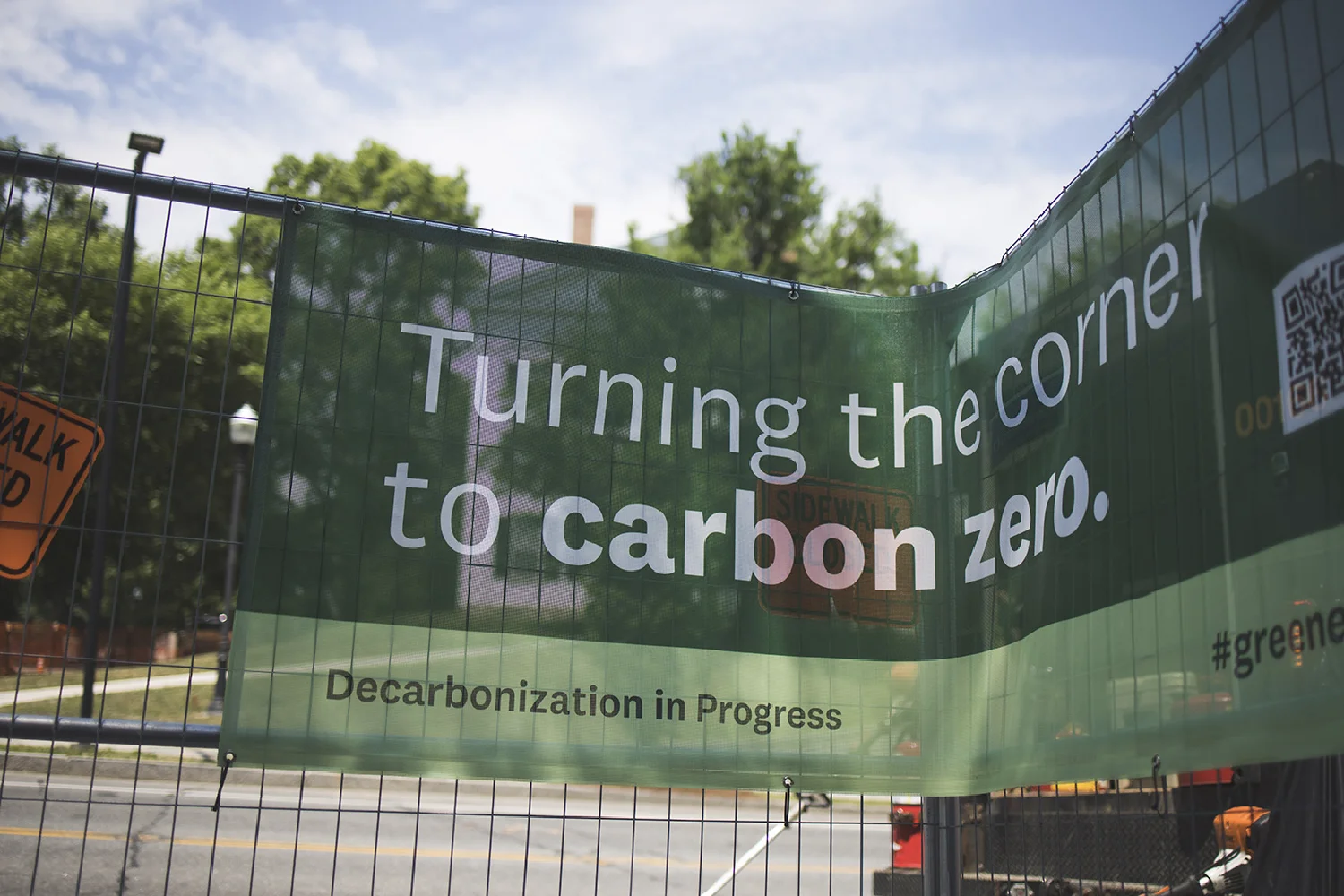 Creative green banner on a fence reads, Turning the corner to carbon zero. Decarbonization in Progress.