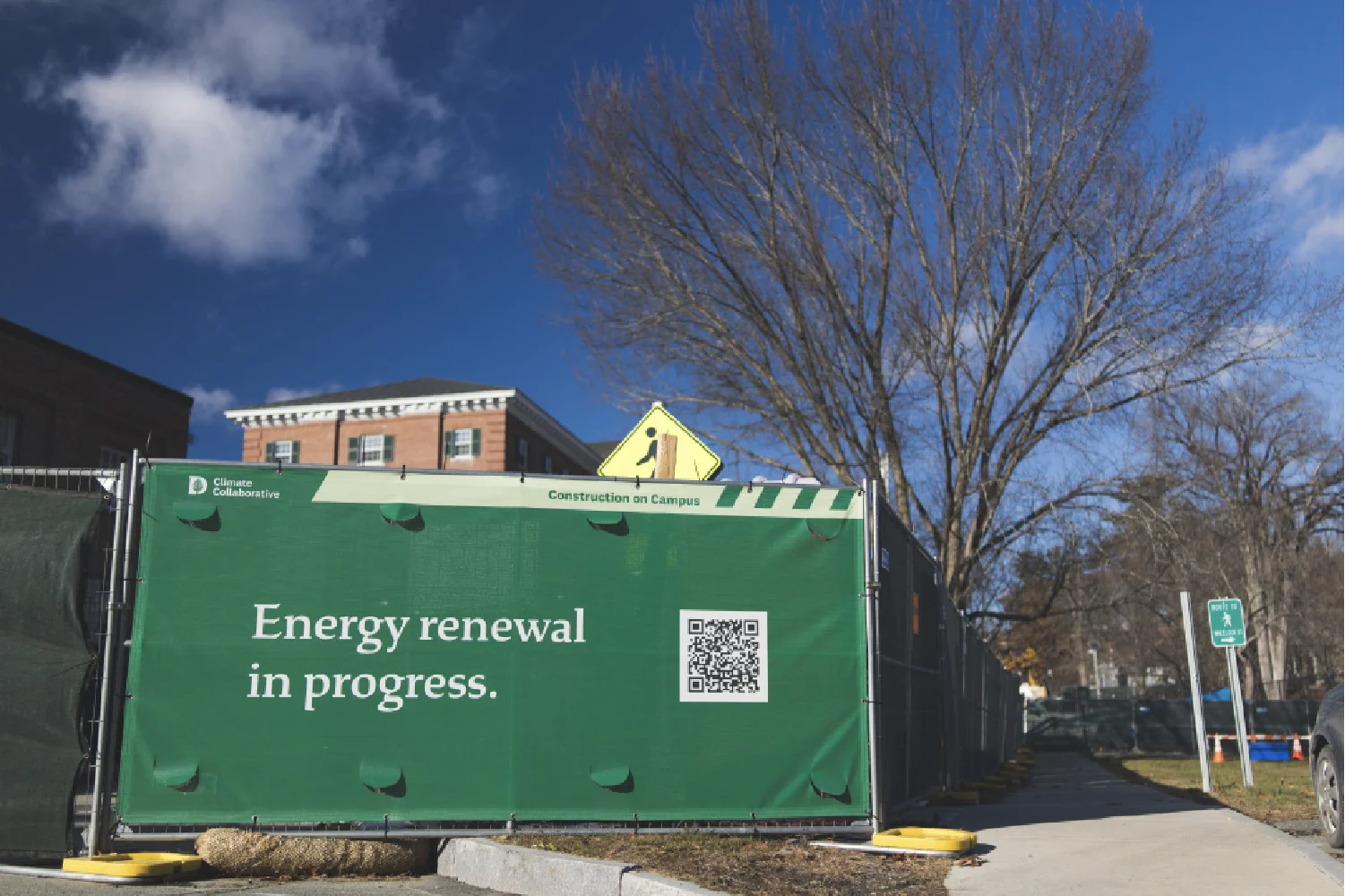 A creative green construction fence reads Energy renewal in progress, with buildings and bare trees visible in the background.