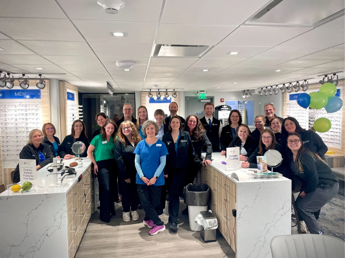 A group of people smiling and posing together inside a modern eyeglass store with displays, balloons, and hints of growth marketing success in the vibrant atmosphere.