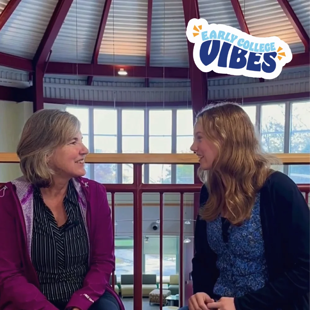 Two women sit indoors talking and smiling under a skylight, sharing early college vibes and growth marketing ideas. Text reads “Early College Vibes” in the corner.