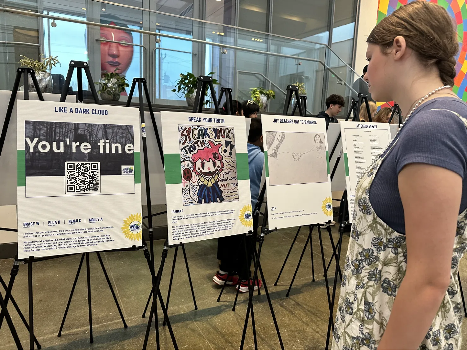A young woman views artwork and posters displayed on easels in a bright indoor gallery space.