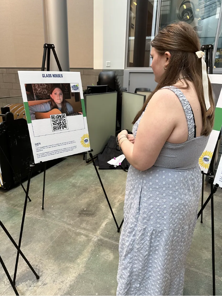 A woman in a gray dress reads a display board featuring a photo and QR code at an indoor exhibit.