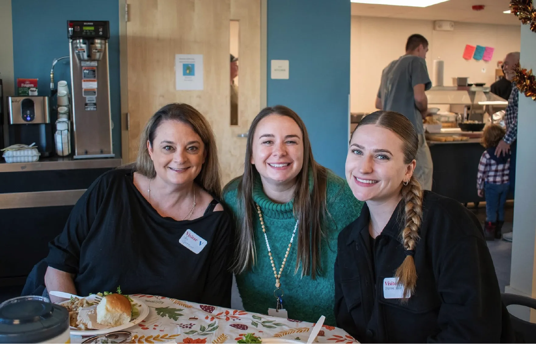 Three women smiling at a decorated table, with food and drinks, in a casual indoor setting.