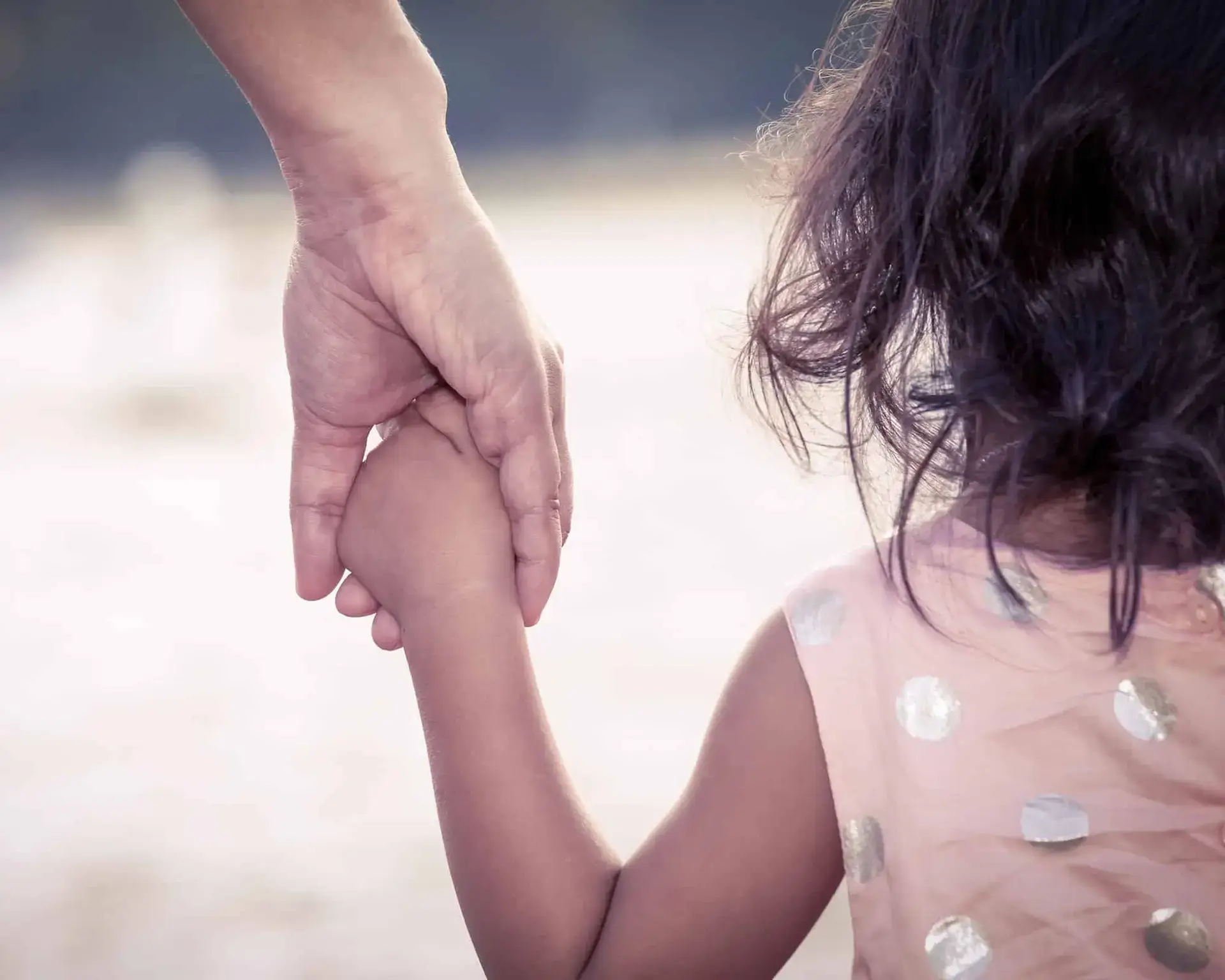 An adult gently holding a young childs hand, offering comfort and support.