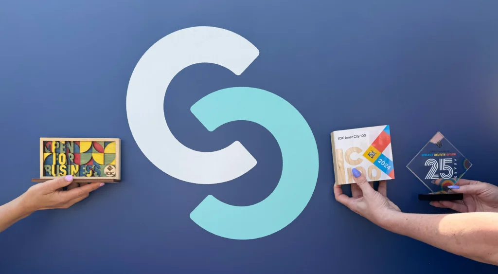 Two hands holding colorful awards in front of a large, stylized CS logo on a blue background.